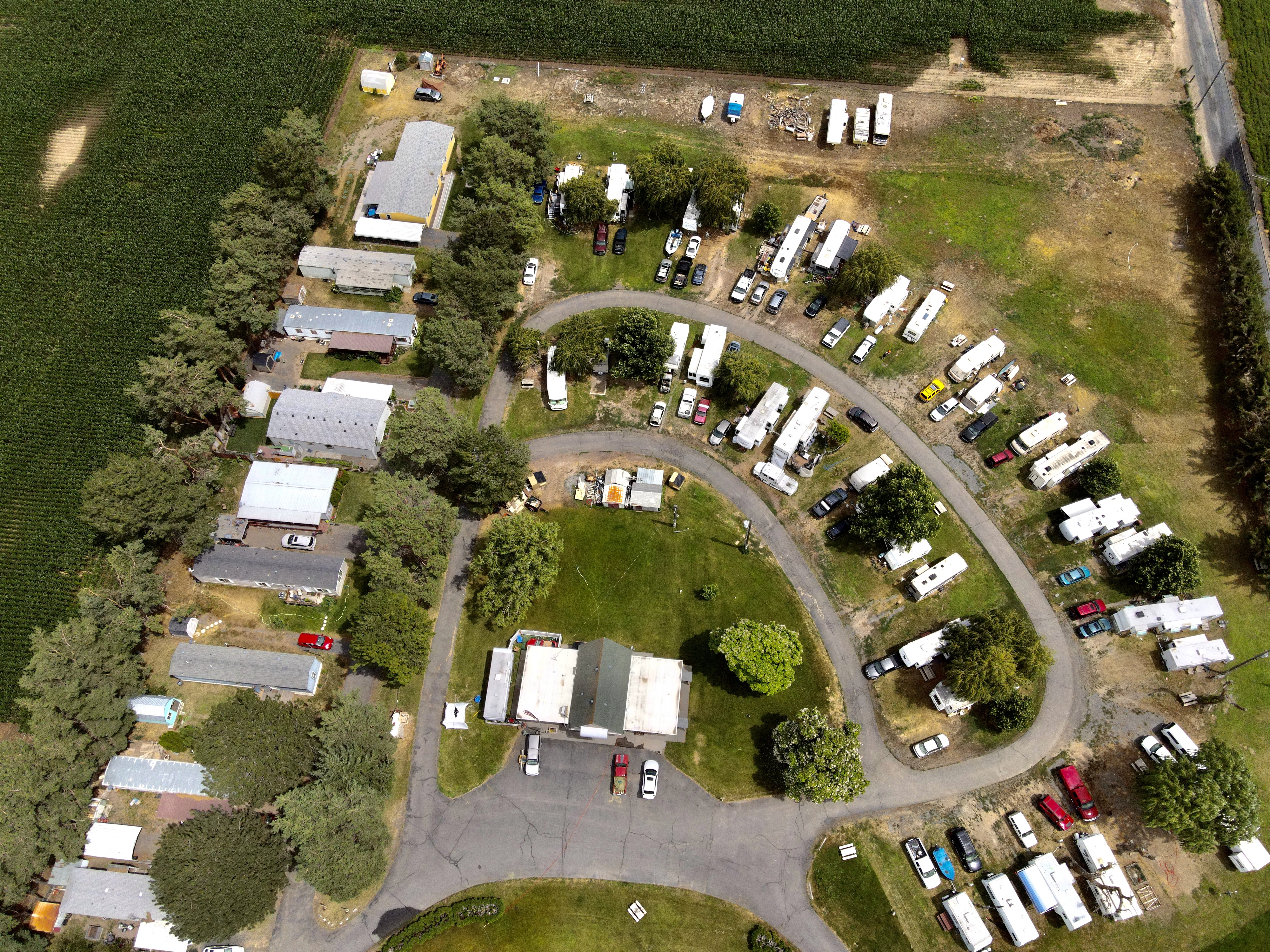 High-angle aerial of Willows Trailer Village showing the interior loop road, long-term RV sites, and manufactured home row beside Moses Lake area farm fields